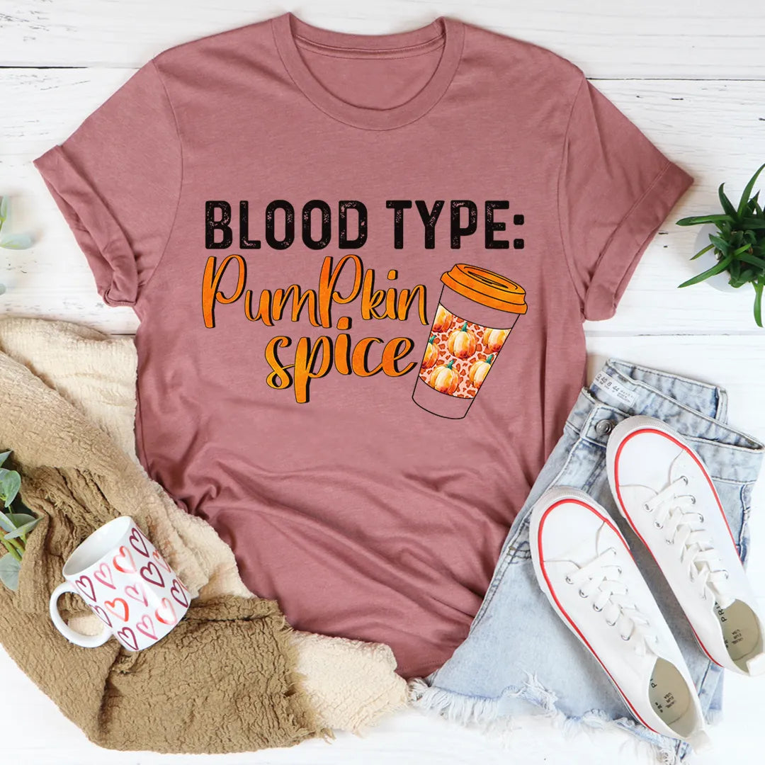 Mauve t-shirt with 'Blood Type: Pumpkin Spice' text and coffee graphic on a white surface with accessories.
