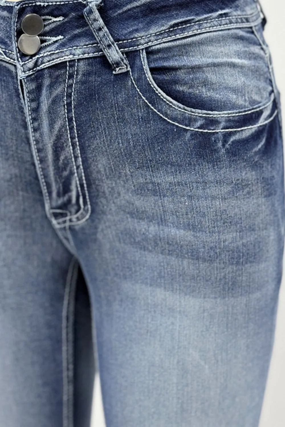 Woman wearing long boot cut acid wash blue jeans with star embroidered pockets, styled with sandals, with dried grass visible in the background.