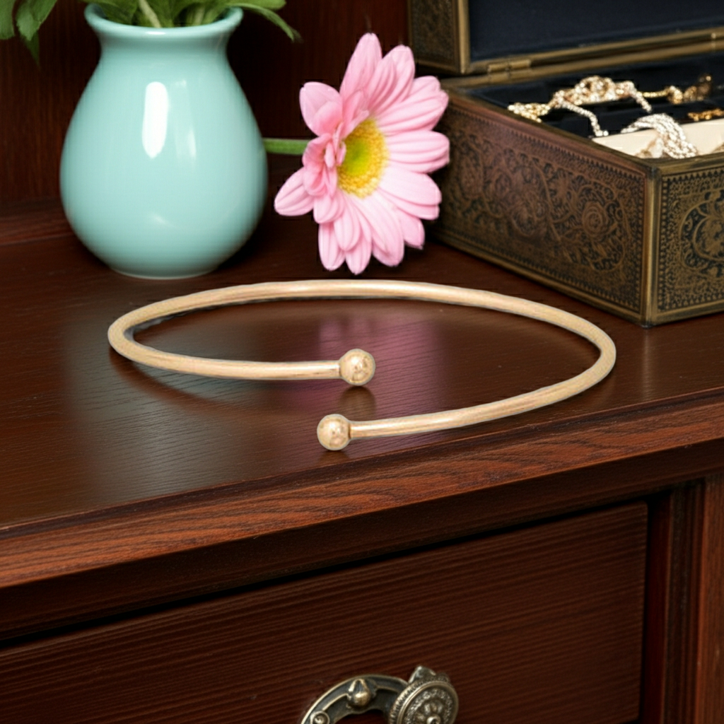 Beige choker necklace on a wooden surface with a pink flower and turquoise vase in the background.