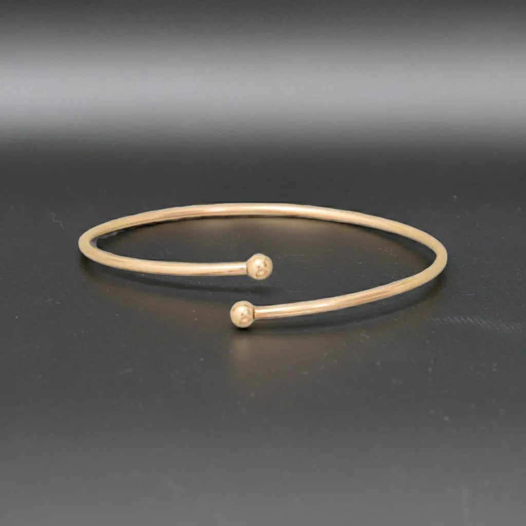 Gold bracelet with two spherical ends on a dark gray background