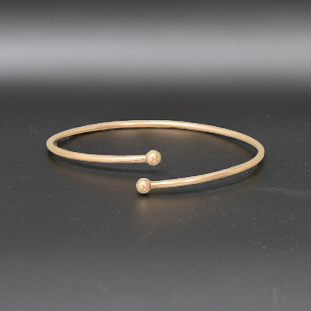Gold bracelet with two small spherical ends on a dark gray background
