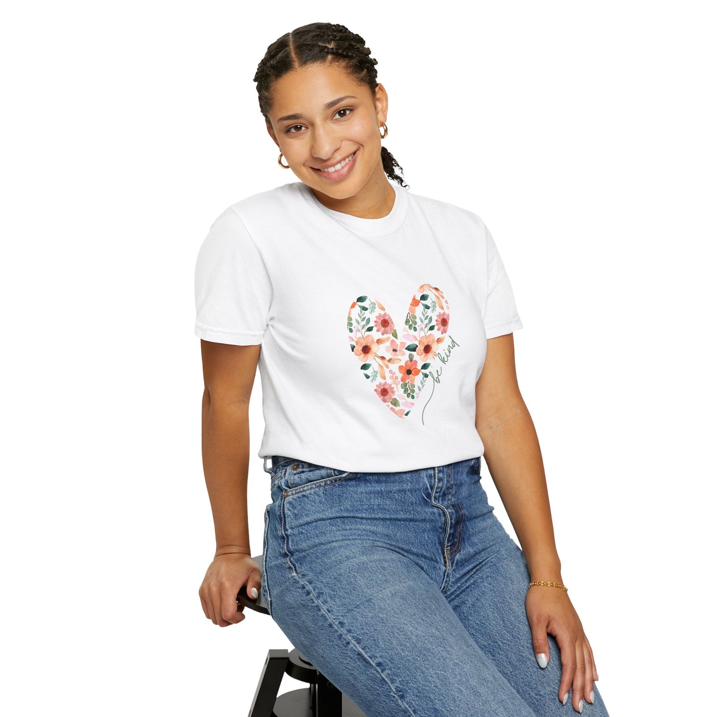 A girl sitting in a chair wearing a white floral heart be kind, graphic tee shirt and jeans.