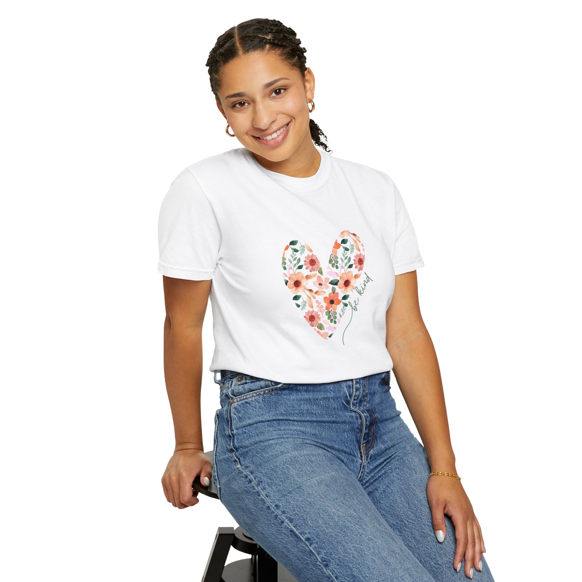 A girl sitting in a chair wearing a white floral heart be kind, graphic tee shirt and jeans.