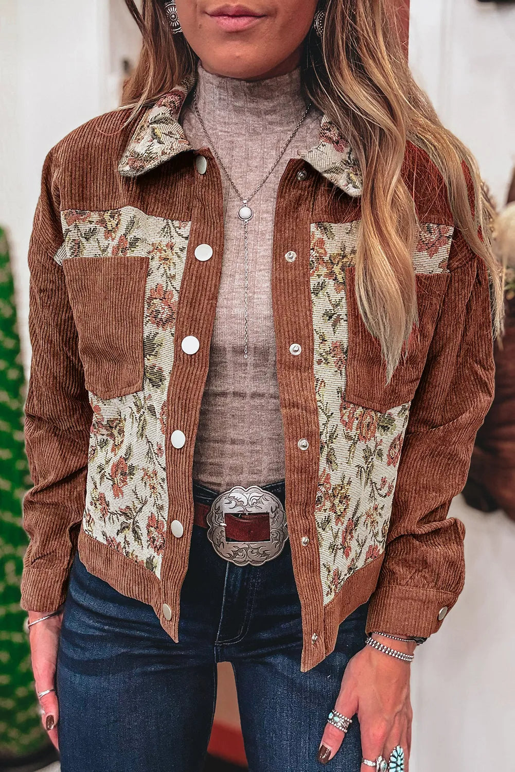 Person wearing a brown floral patchwork jacket with a neutral background