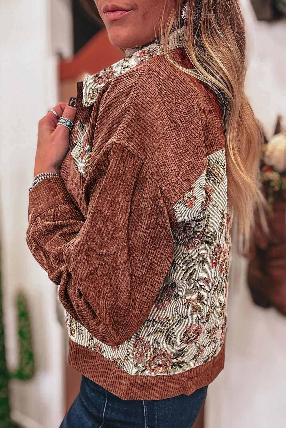 Women standing with a side view of a brown ribbed floral patch work long sleeve jacket.