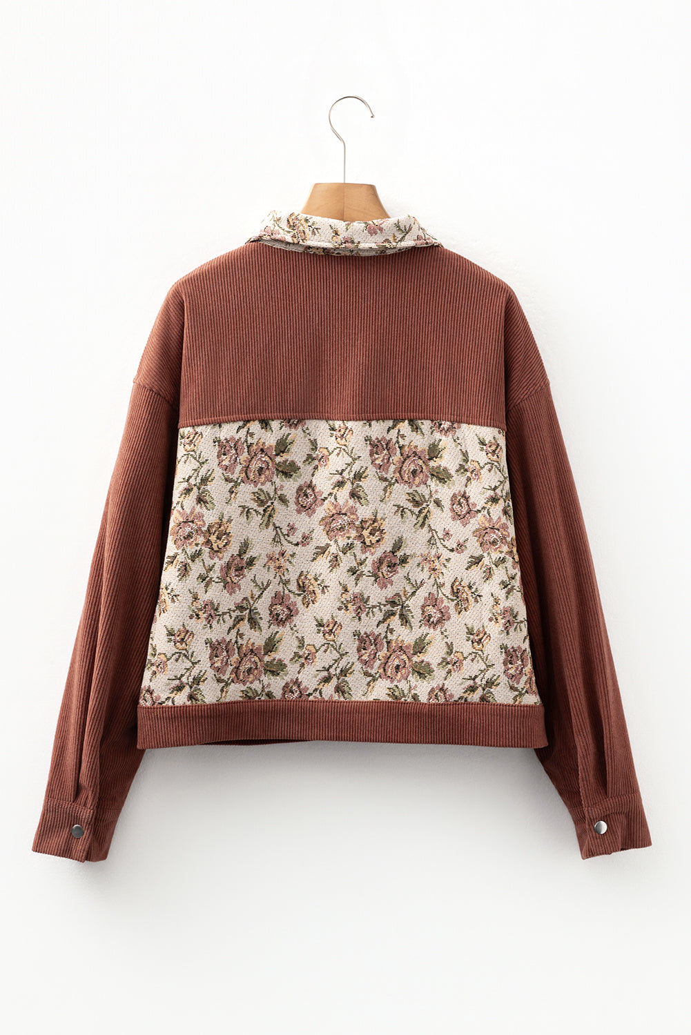 A back side view of a long sleeve ribbed brown jacket with floral patchwork on a wooden hanger.
