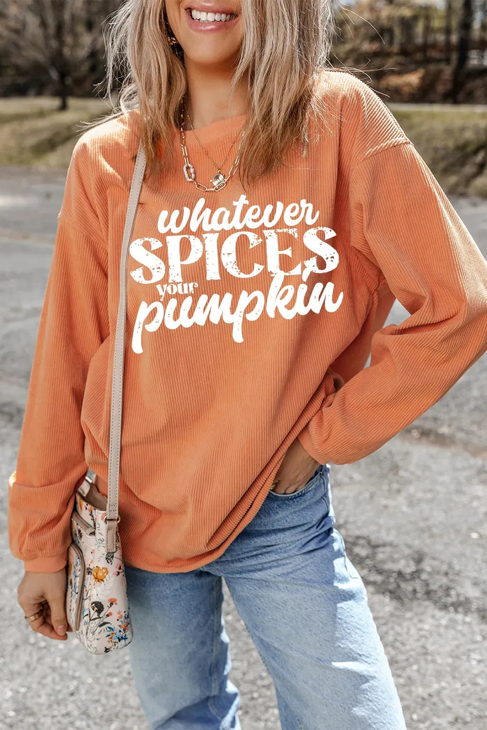 Person wearing an orange sweatshirt with text, standing outdoors.