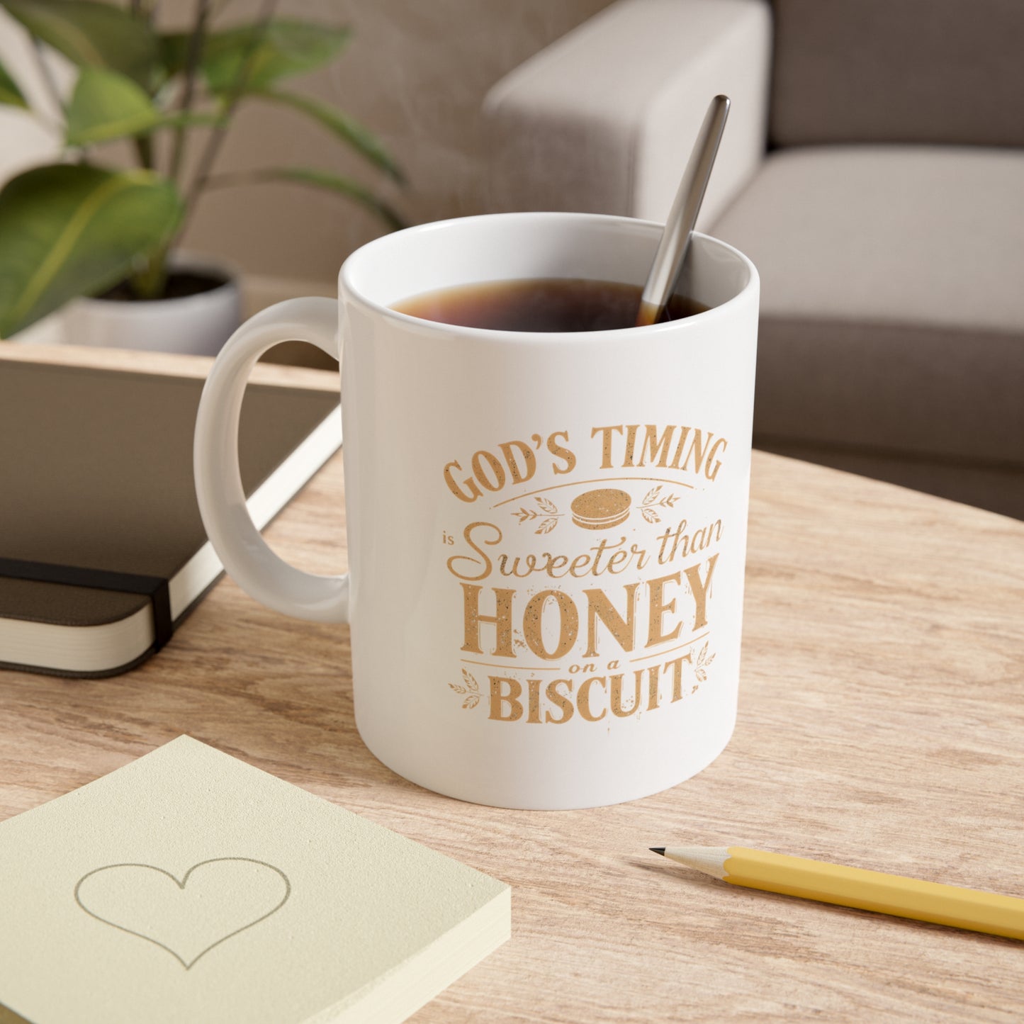 White mug with text on a wooden table with a plant and book in the background