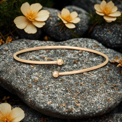 Gold bracelet on a stone surface with small flowers in the background