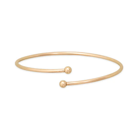Gold bangle with two spherical ends on a white background