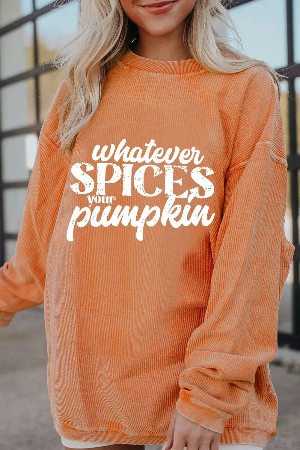 Person wearing an orange sweatshirt with text 'Whatever spices your pumpkin' in a casual setting.