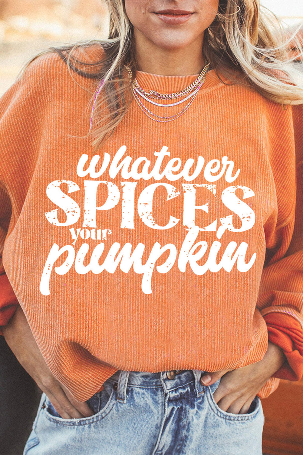 Person wearing an orange sweater with 'Whatever Spices Your Pumpkin' text.