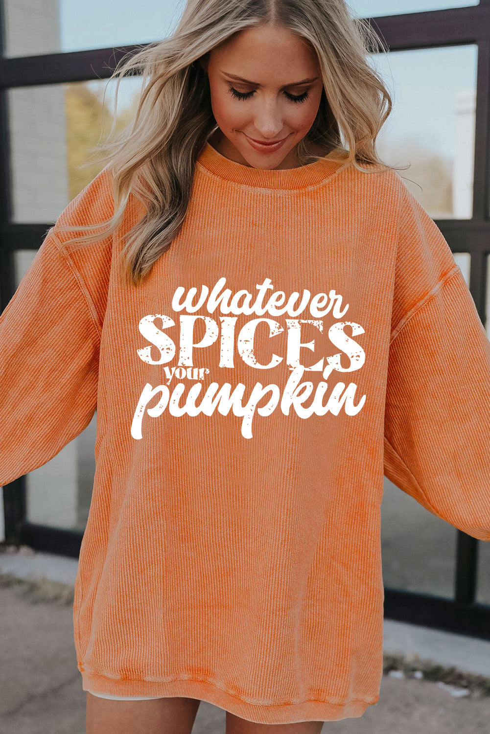 Person wearing an orange sweater with text 'whatever SPICES your pumpkin' in a casual setting.