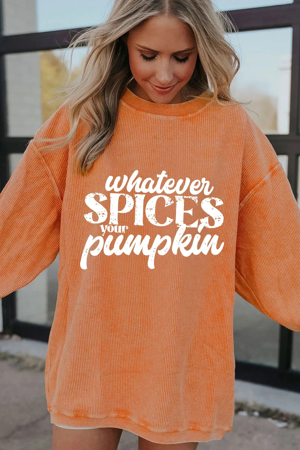 Person wearing an orange sweatshirt with text 'whatever SPICES your pumpkin' in a casual setting.