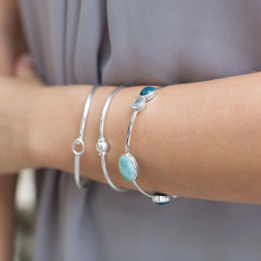 Close-up of a person's wrist wearing multiple silver bracelets with turquoise stones on a blurred background.