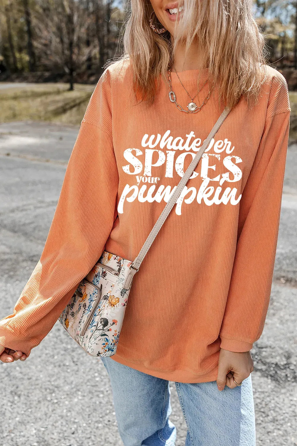 Person wearing an orange sweatshirt with text, holding a patterned bag outdoors.