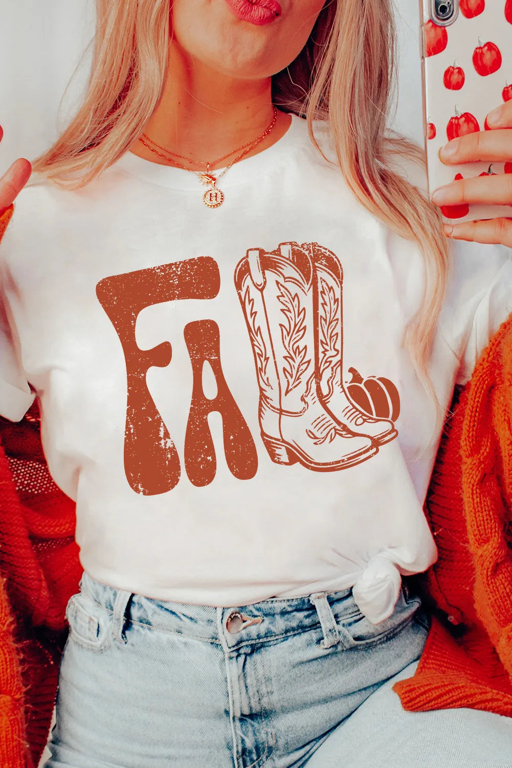 Person wearing a white t-shirt with 'FALL' and cowboy boot design, holding a phone with a red case.