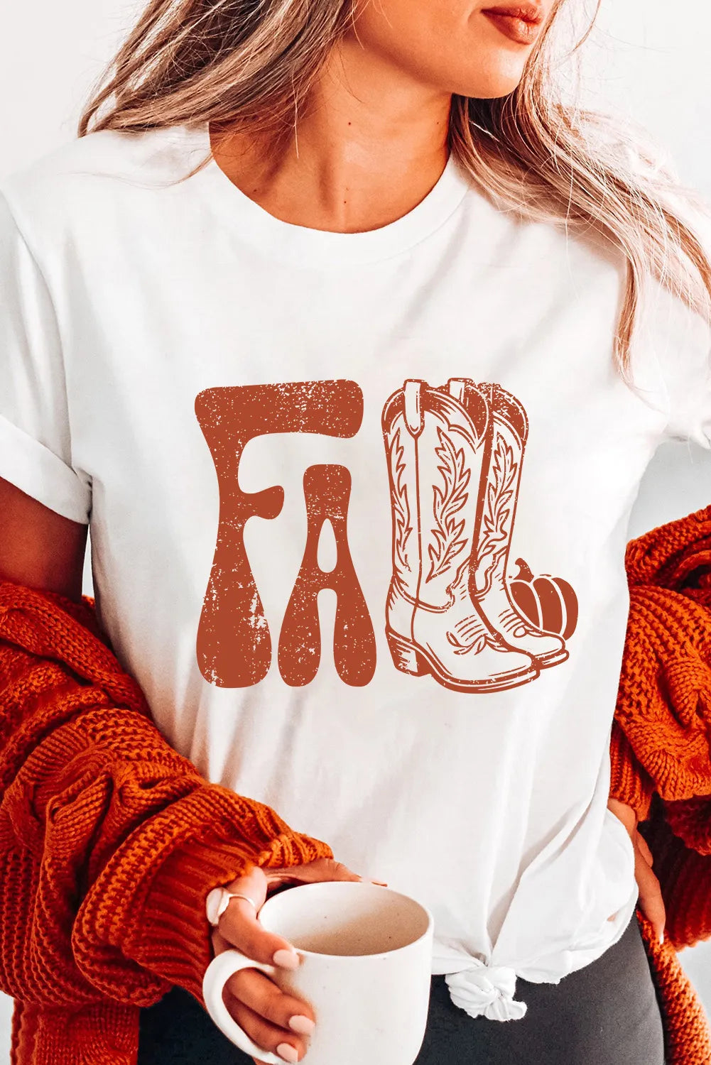 Person wearing a white shirt with cowboy boot and 'FA' design, holding a mug.