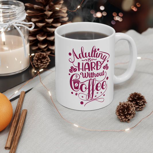 White mug with 'Adulting is hard without coffee' text, surrounded by decorative items on a table.