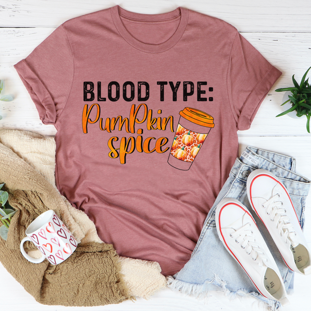 Mauve t-shirt with 'Blood Type: Pumpkin Spice' text and coffee graphic, surrounded by casual items on a light wooden surface.