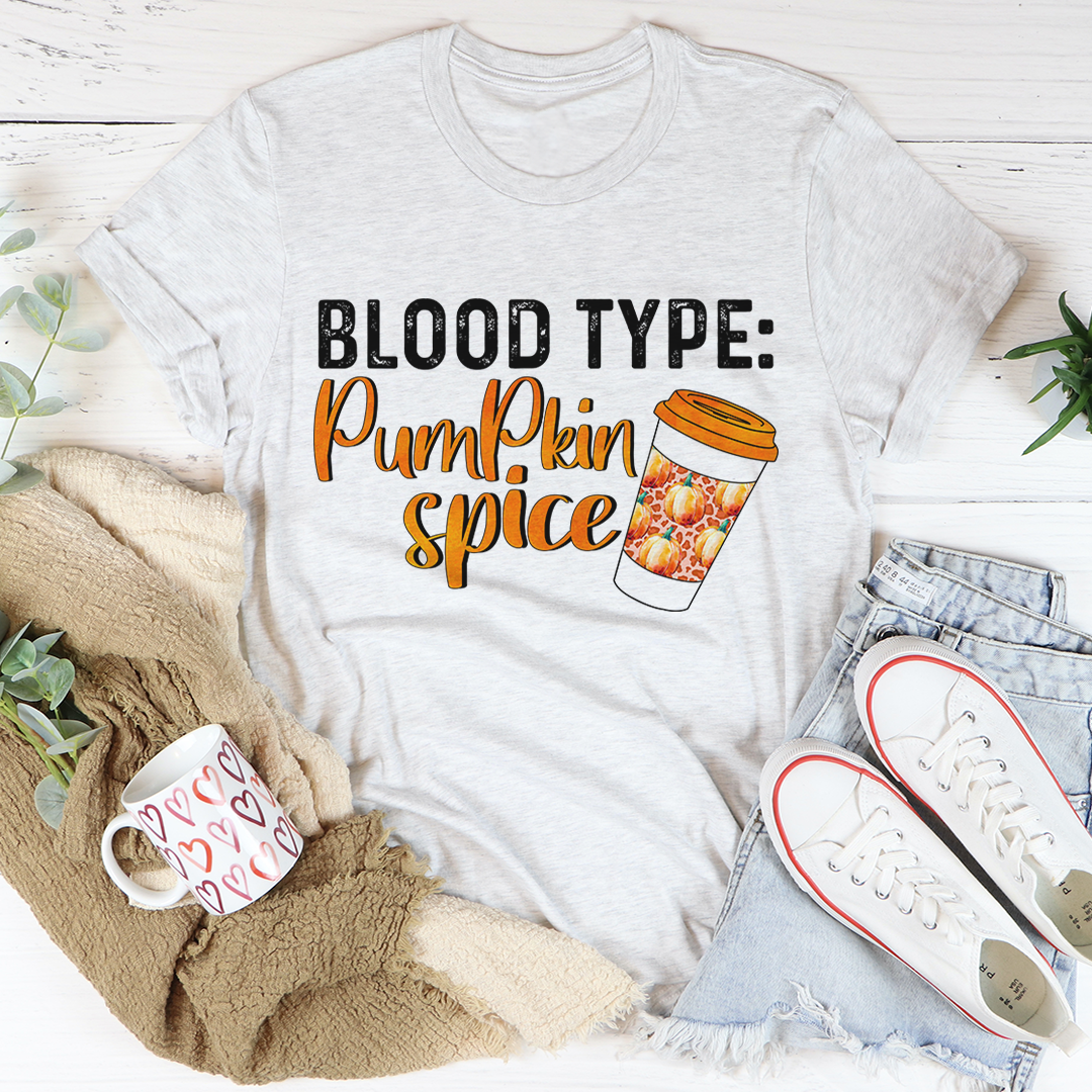 White t-shirt with 'Blood Type: Pumpkin Spice' design on a white surface with accessories.