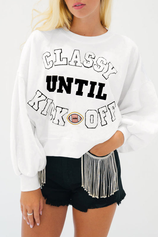 Person wearing a white sweatshirt with text and black shorts with fringe.