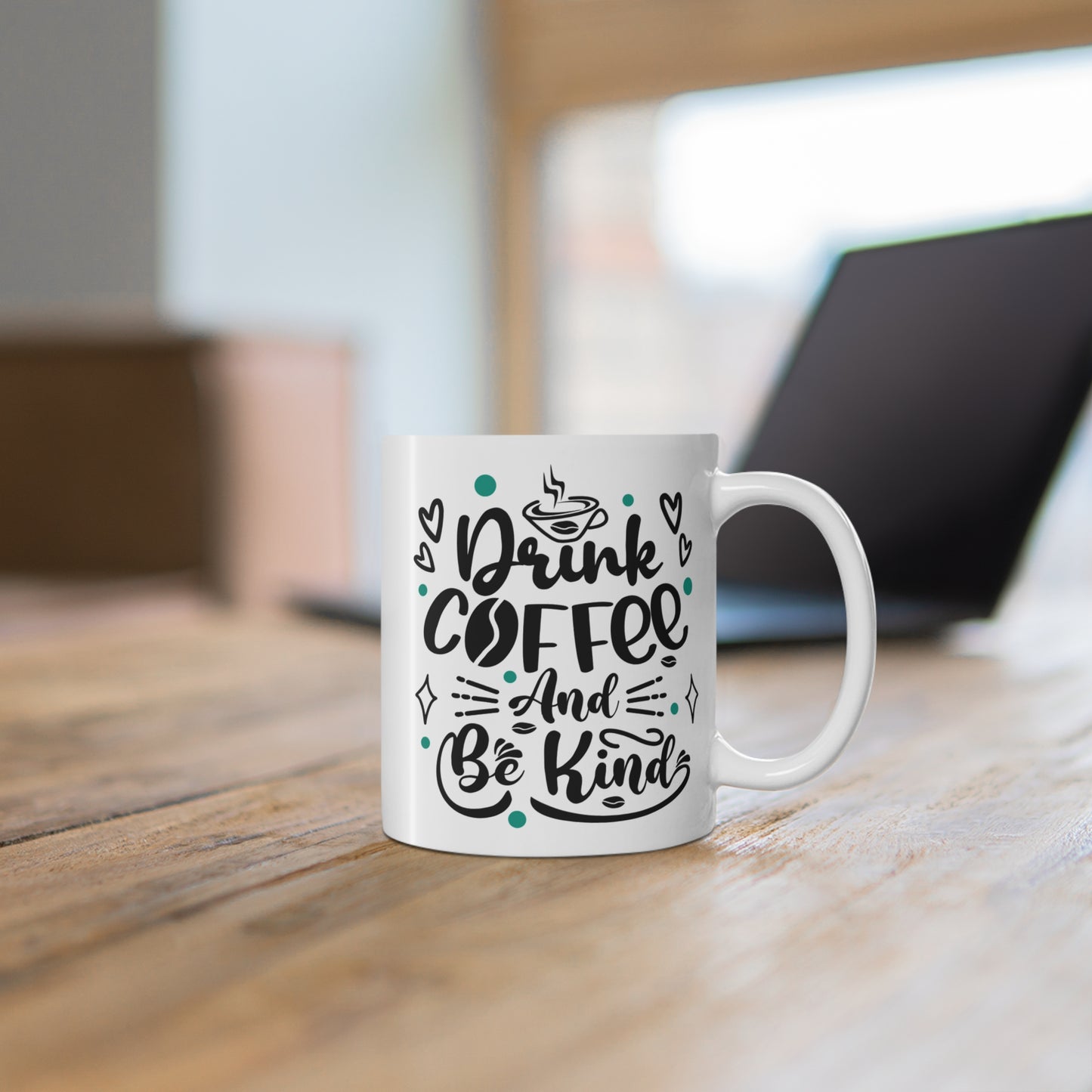 White mug with 'Drink Coffee And Be Kind' text on a wooden desk.