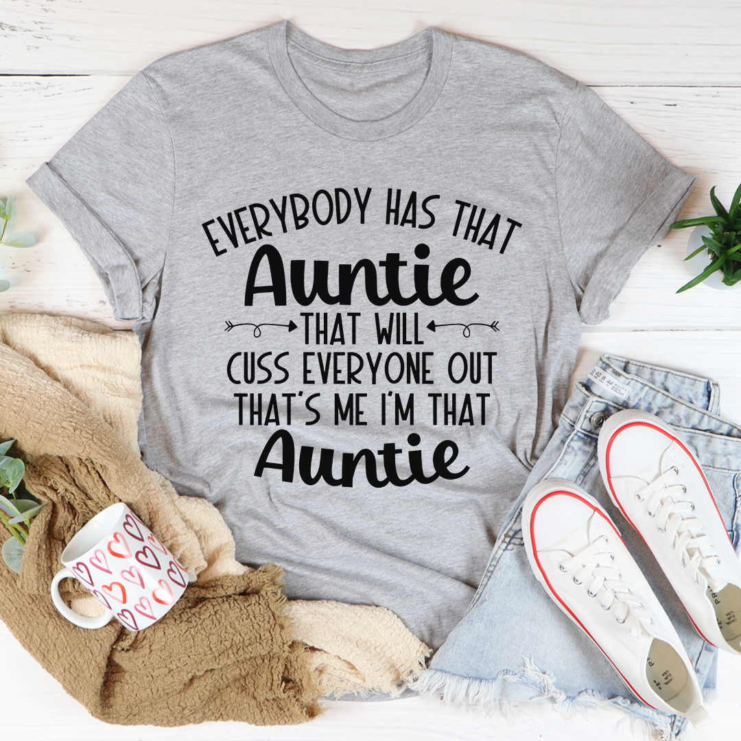 Gray t-shirt with humorous text design on a white surface with casual items around
