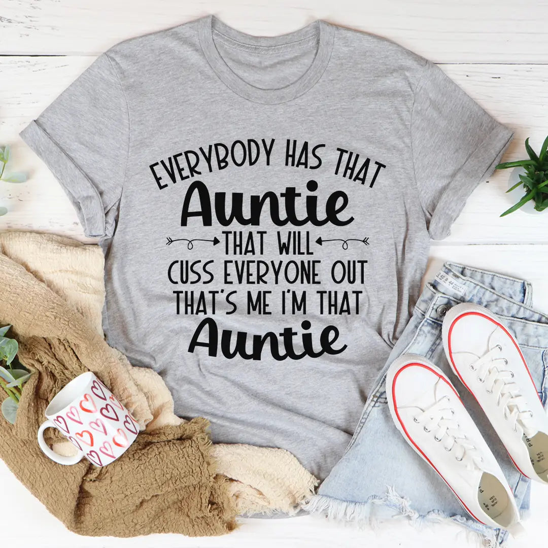 Gray t-shirt with humorous text design on a white surface with casual items around