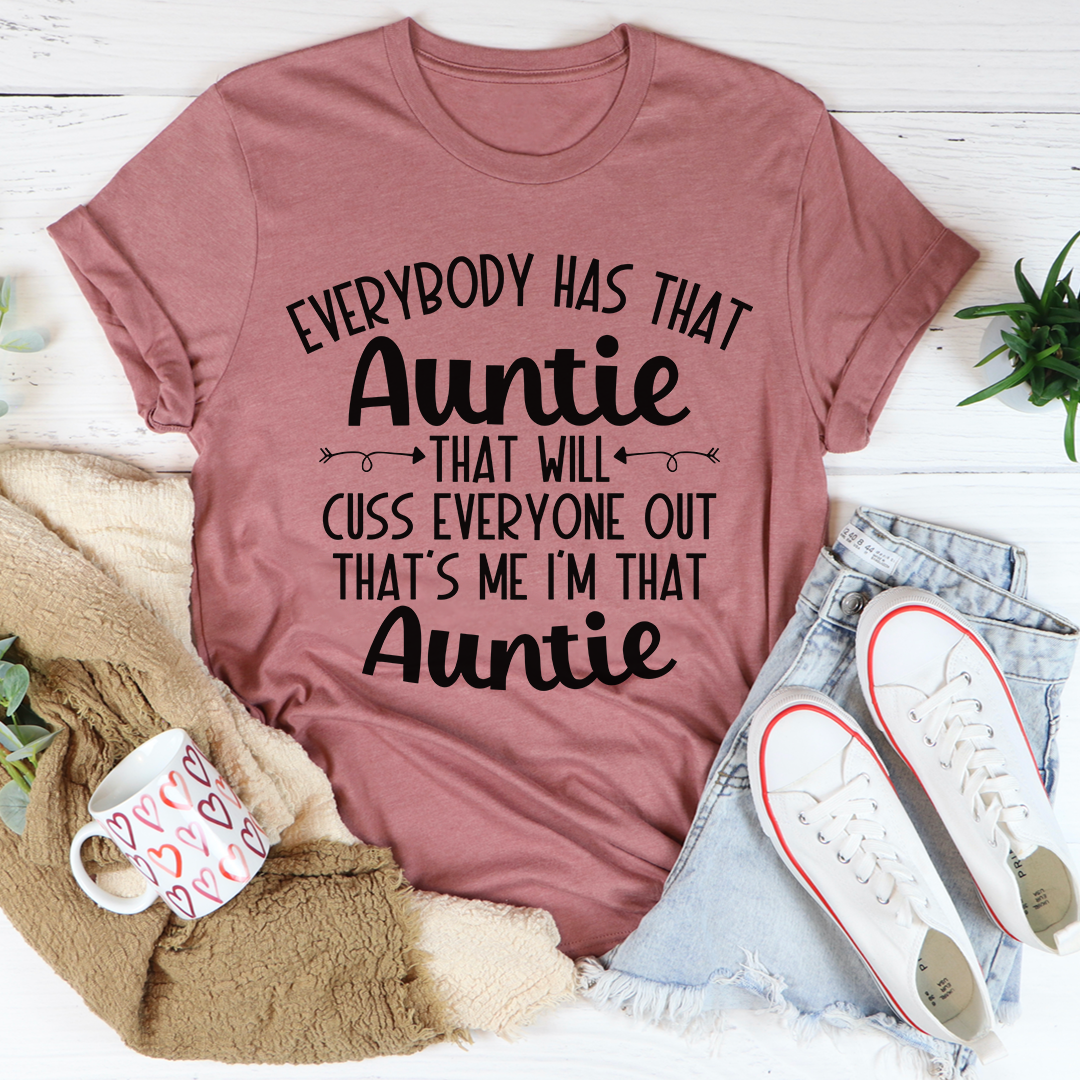 Mauve t-shirt with humorous text on a white surface with casual items around