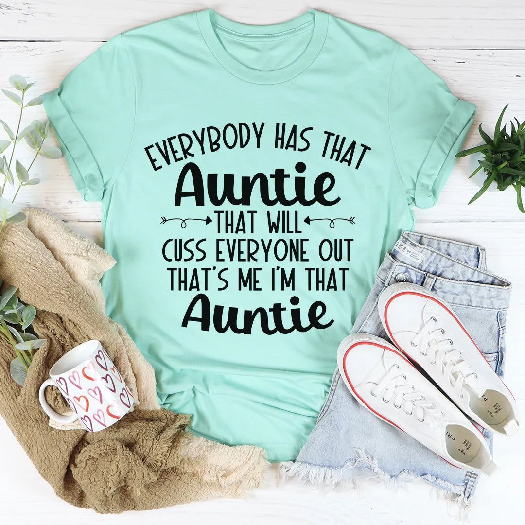 Mint green t-shirt with humorous text, placed on a white surface with shoes, mug, and plants.