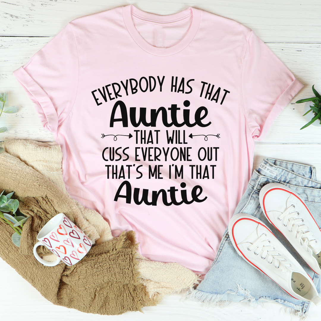 Pink t-shirt with humorous text design on a light wooden surface with casual items.