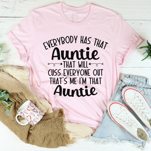 Pink t-shirt with humorous text design on a light wooden surface with casual items.