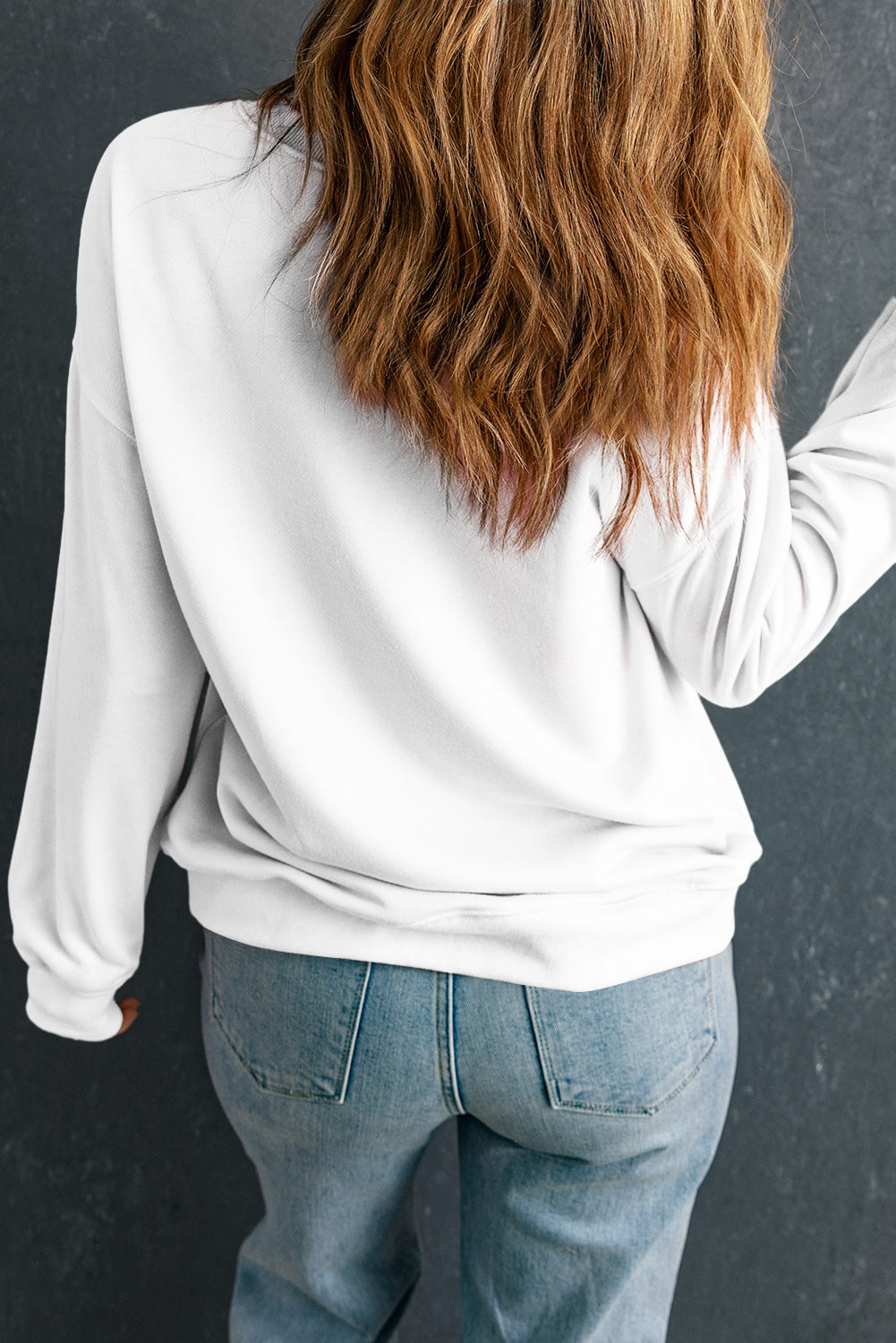 Person wearing a white long-sleeve top and blue jeans against a dark background