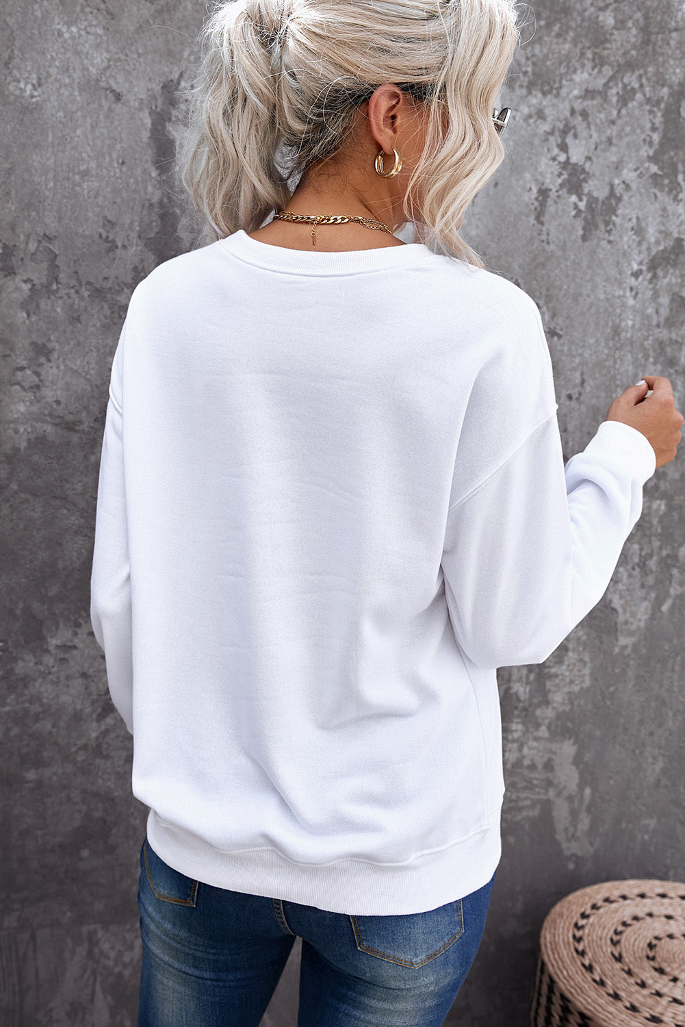Person wearing a white sweatshirt against a gray wall