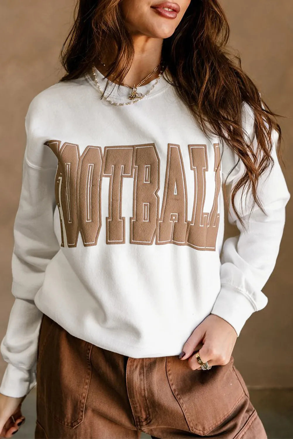 Person wearing a white sweatshirt with 'FOOTBALL' printed in brown letters against a beige background
