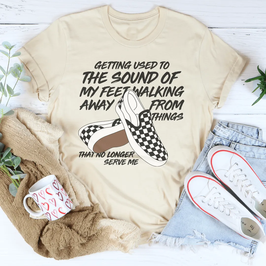Beige t-shirt with graphic and text, placed on a white surface with jeans and shoes.