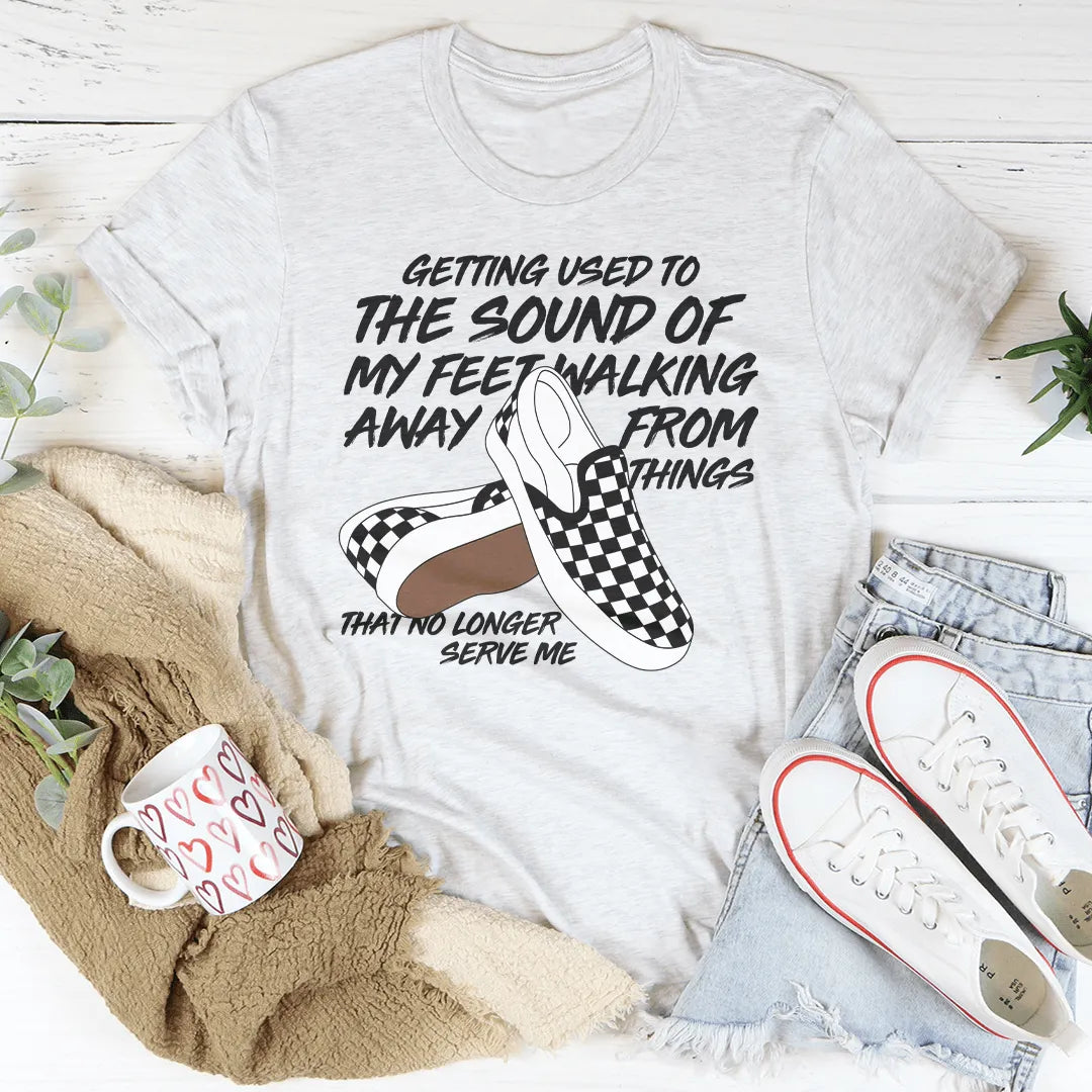White t-shirt with graphic and text, placed on a surface with shoes and a mug.