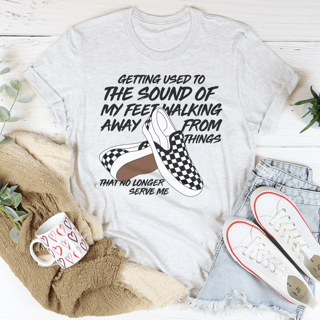 White t-shirt with graphic and text, placed on a surface with shoes and a mug.