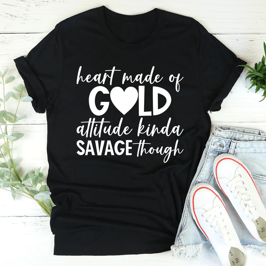Black t-shirt with white text 'heart made of gold, attitude kinda savage though' on a light wooden surface with shoes and plants.