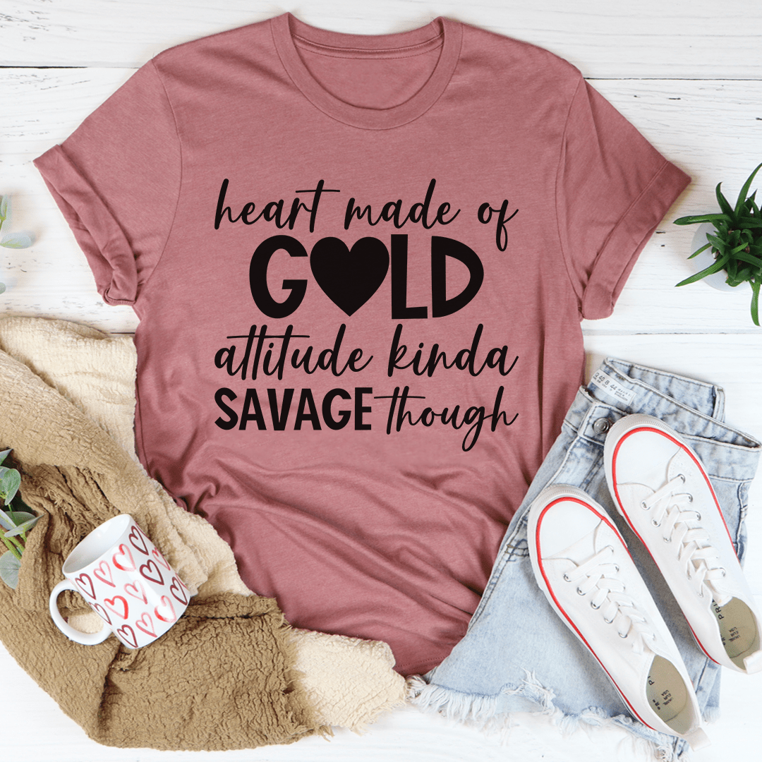 Mauve t-shirt with text 'heart made of gold, attitude kinda savage though' on a white surface with casual items.