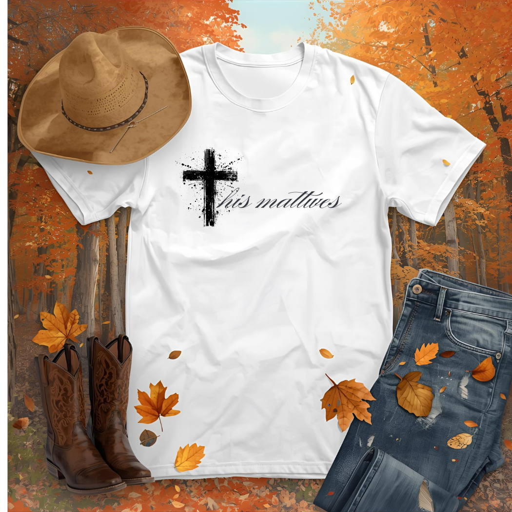 White t-shirt with cross and text design, cowboy hat, boots, and jeans on an autumn-themed background.