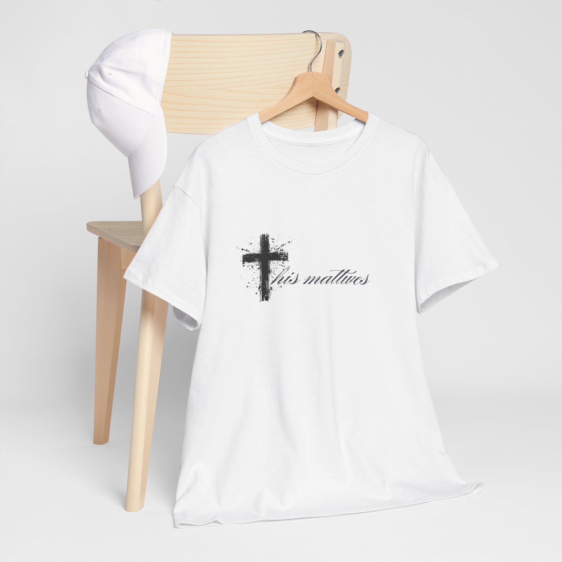 White t-shirt with a black cross and text on a wooden chair against a white background