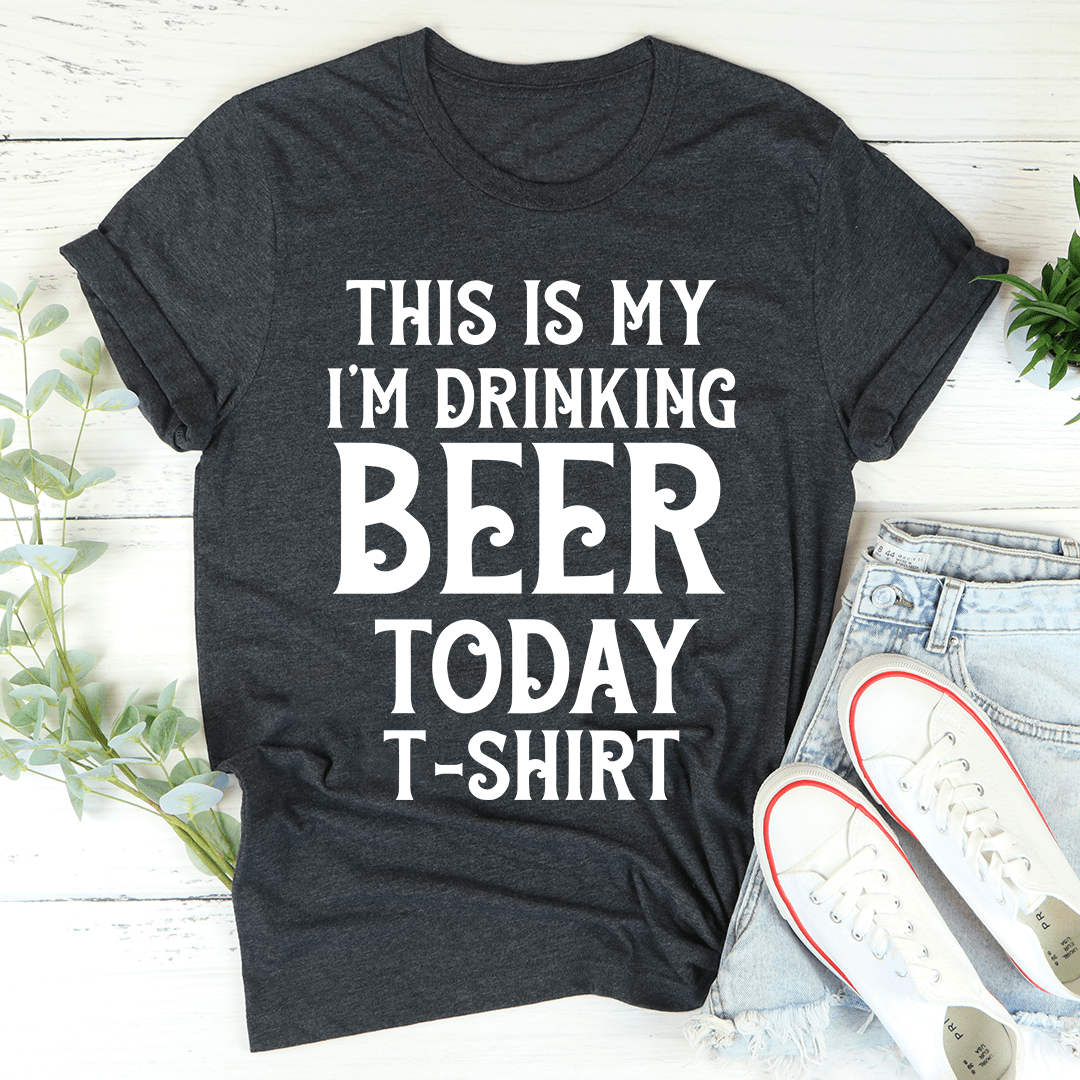 Dark gray t-shirt with white text 'This is my I'm drinking beer today t-shirt' on a light wooden surface.