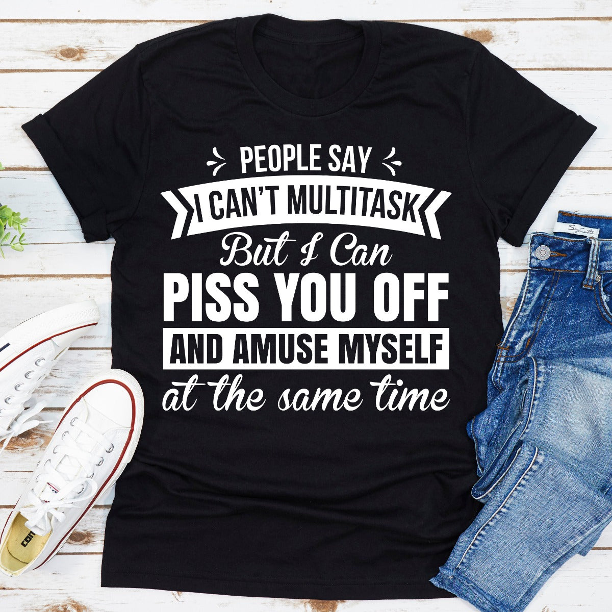 Black t-shirt with humorous text design on a wooden surface with jeans and sneakers.