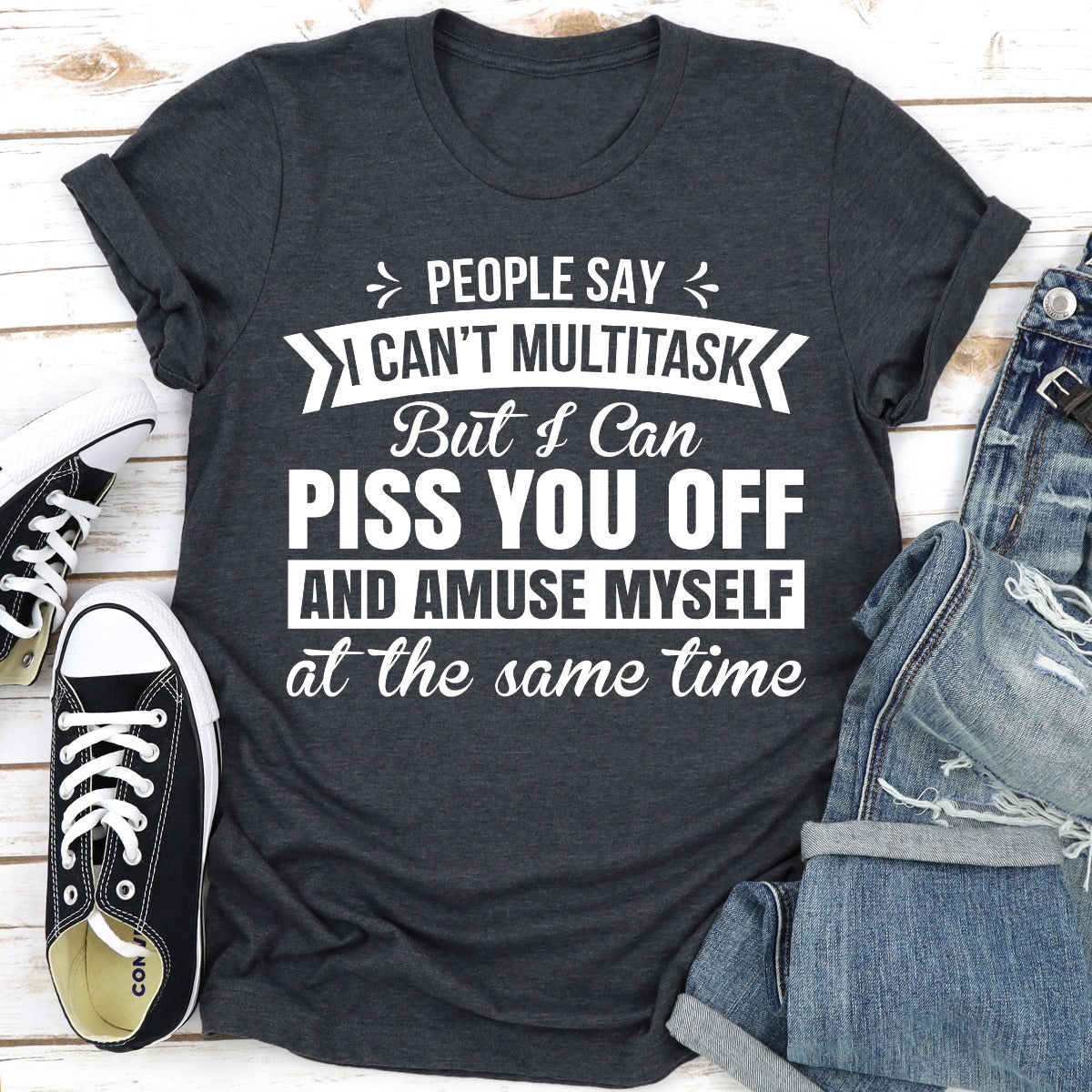 Dark gray t-shirt with humorous text design on a wooden surface with shoes and jeans.