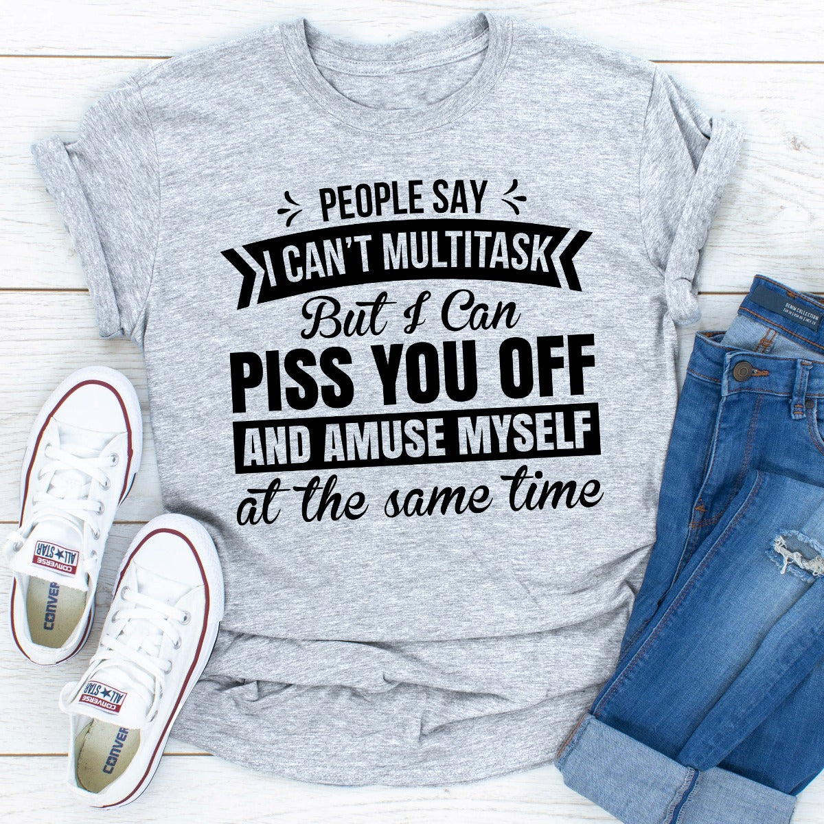 Gray t-shirt with humorous text design on a wooden surface with shoes and jeans.