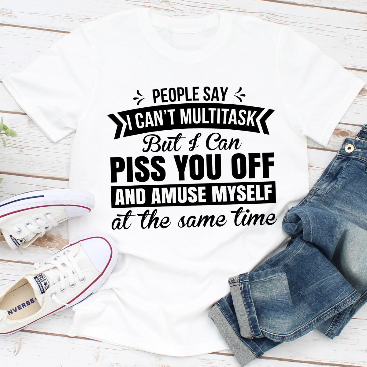 White t-shirt with humorous text design on a wooden surface with jeans and sneakers.