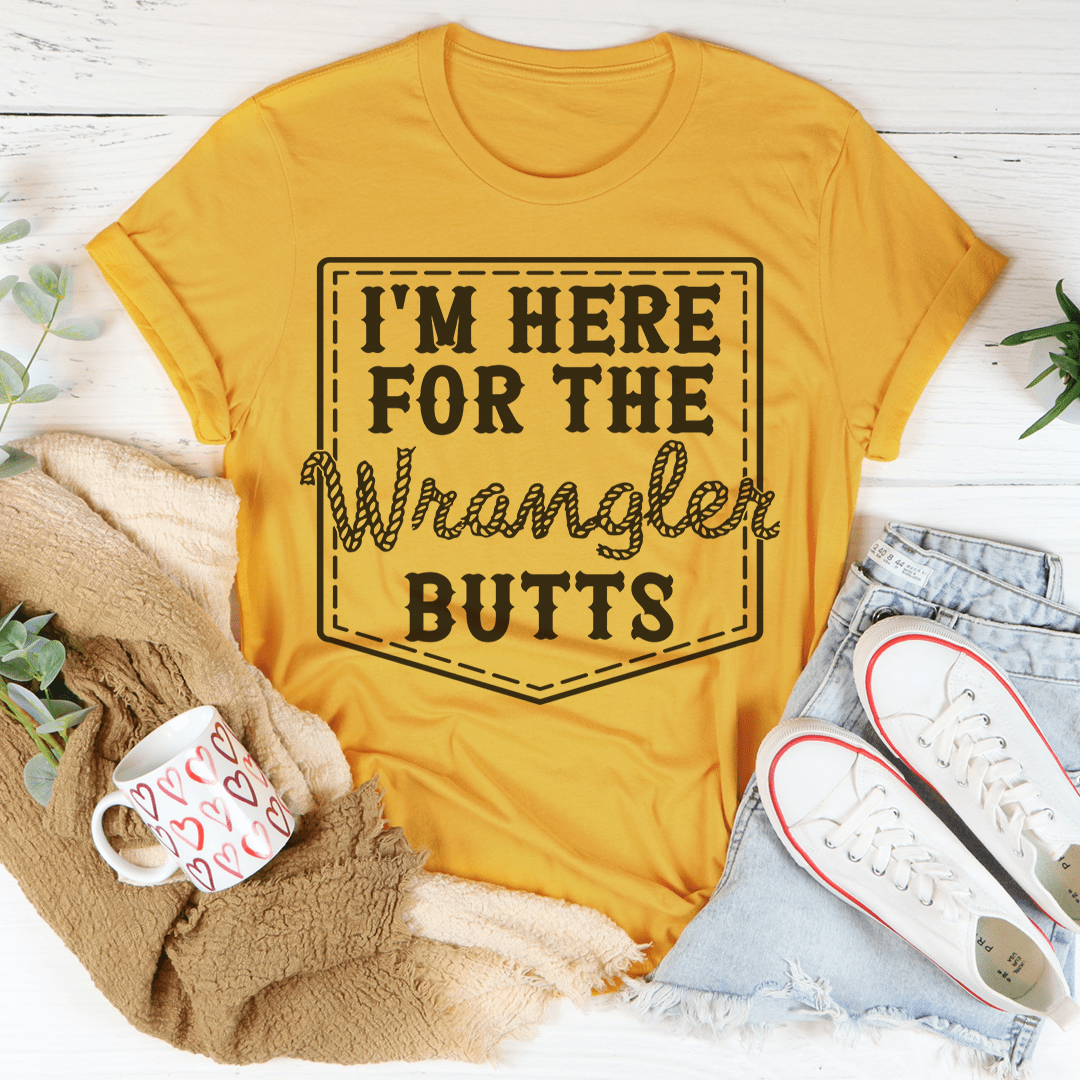 Yellow t-shirt with 'I'm here for the Wrangler Butts' text on a white surface with casual items.