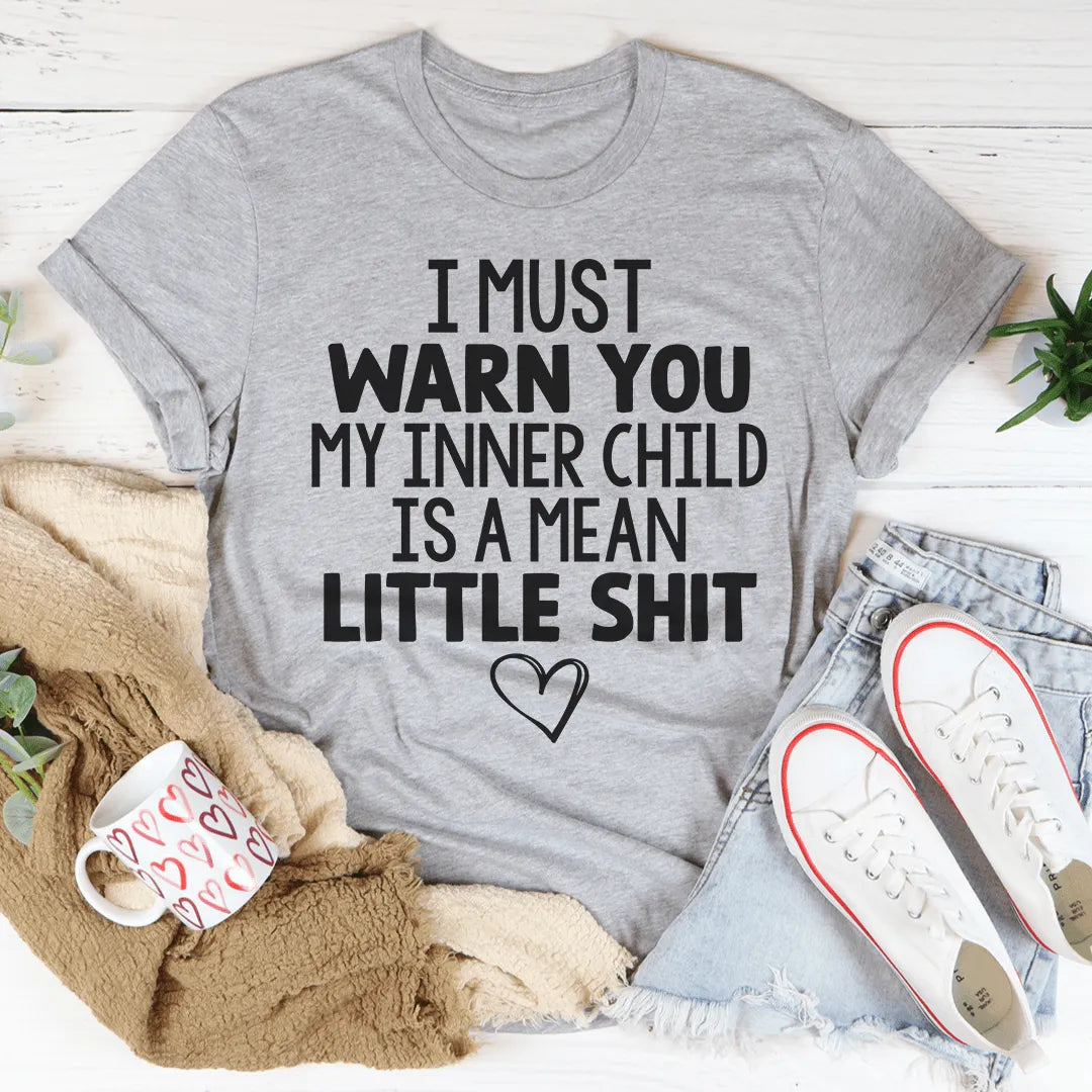 Gray t-shirt with humorous text on a white surface with casual items around